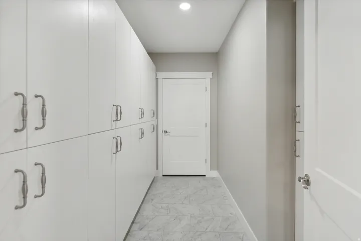 Extended hallway featuring a full wall of floor-to-ceiling white cabinetry with decorative pulls, recessed ceiling lighting, and grey tiled flooring