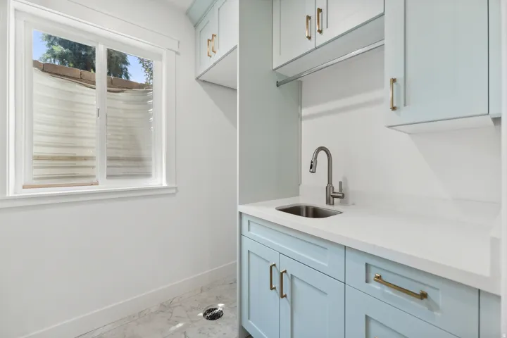 Utility room featuring light blue cabinetry with gold-finish hardware, a stainless steel sink, and a white countertop