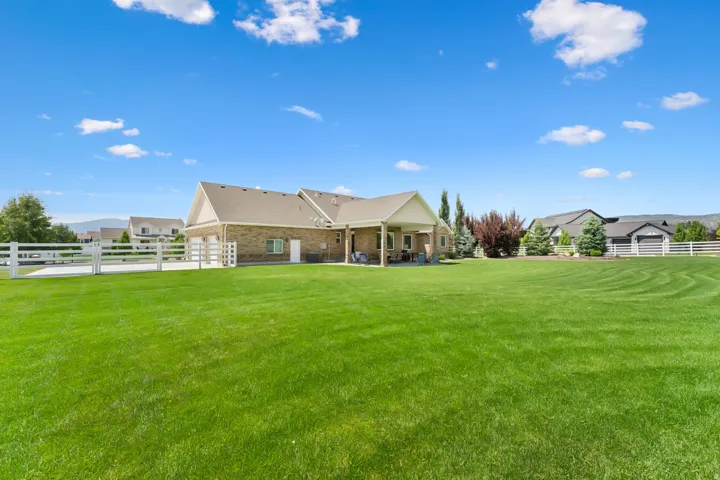 Expansive green lawn with a white fence, featuring a brick-sided residence with a covered patio