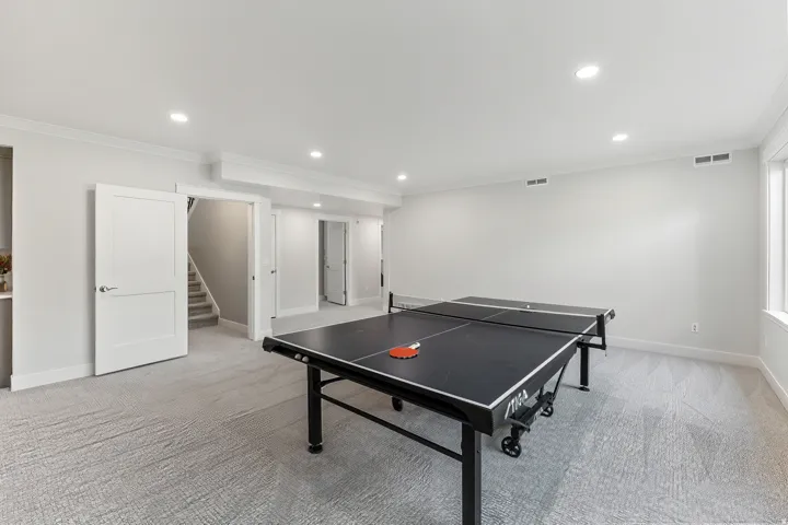 Spacious interior room with light gray patterned carpet, white walls, recessed lighting, and crown molding