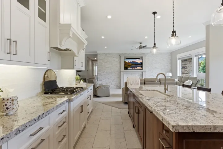 Gourmet kitchen featuring white shaker cabinetry, stone countertops, a tile backsplash, a gas range, and a spacious island with an undermount sink and pendant lighting