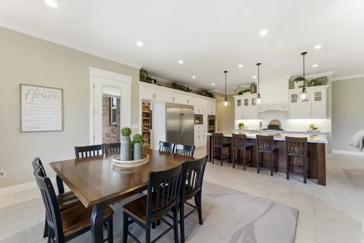Open-concept kitchen and dining area featuring recessed lighting, a large island with seating, pendant lighting, white cabinetry, and stainless steel appliances
