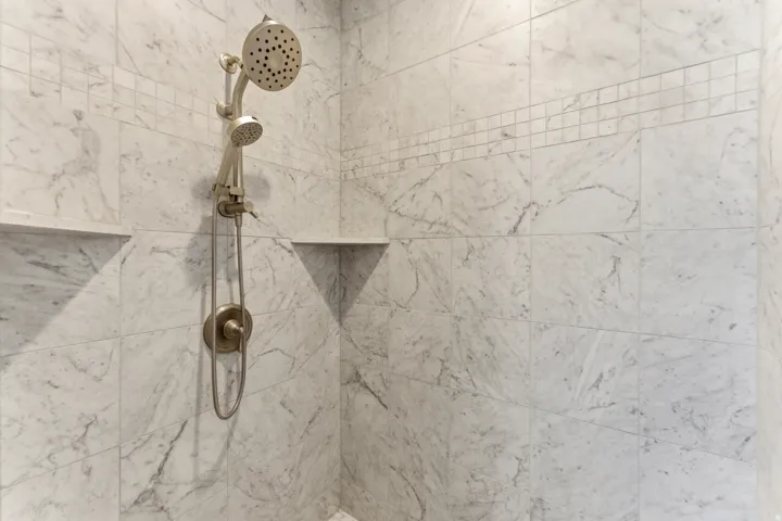 Shower featuring large format marble-look tile, mosaic accent band, brushed nickel shower fixtures, rain showerhead, and two recessed shelving niches