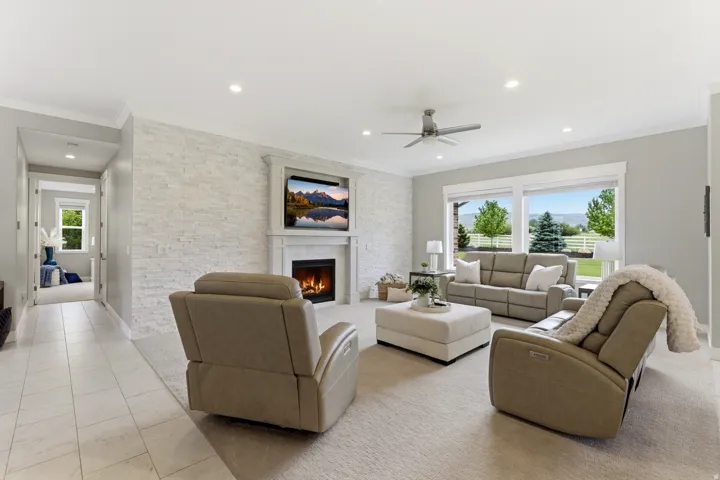 Living area featuring a stone accent wall, an integrated fireplace with mantel, recessed lighting, and a ceiling fan