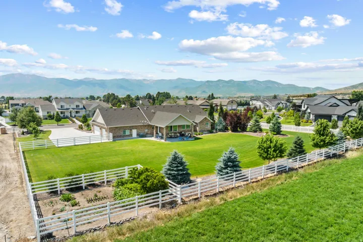Expansive green lawn with mature trees and a white picket fence, backed by mountain scenery