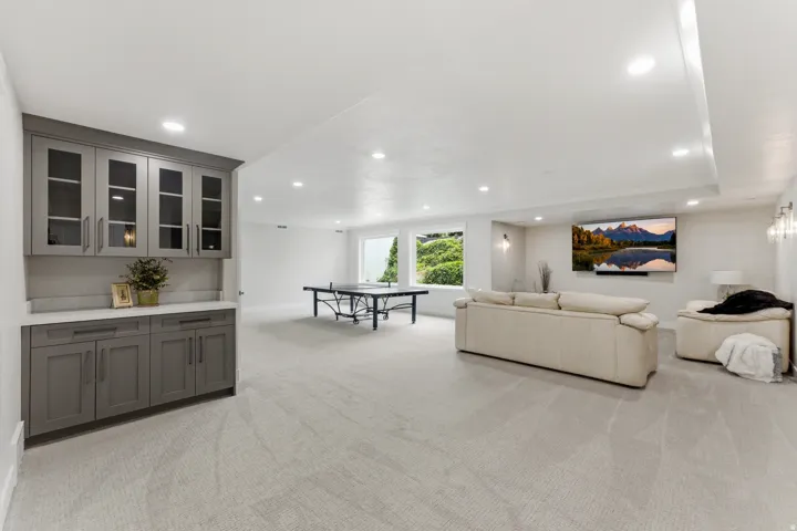 Spacious open-concept room with recessed lighting, built-in cabinetry featuring glass inserts and a light-toned countertop, multiple windows, and light-toned carpeting