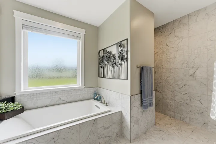 Soaking tub with a large window, complemented by marble-finish tile surrounding the tub and extending into the shower area