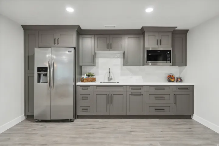 Kitchenette featuring grey shaker-style cabinetry, white countertops, a stainless steel side-by-side refrigerator, a stainless steel microwave, and wood-finish flooring