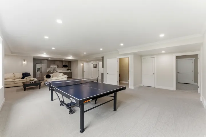 Expansive recreation room featuring light-toned carpet flooring, recessed lighting, and multiple white paneled doors