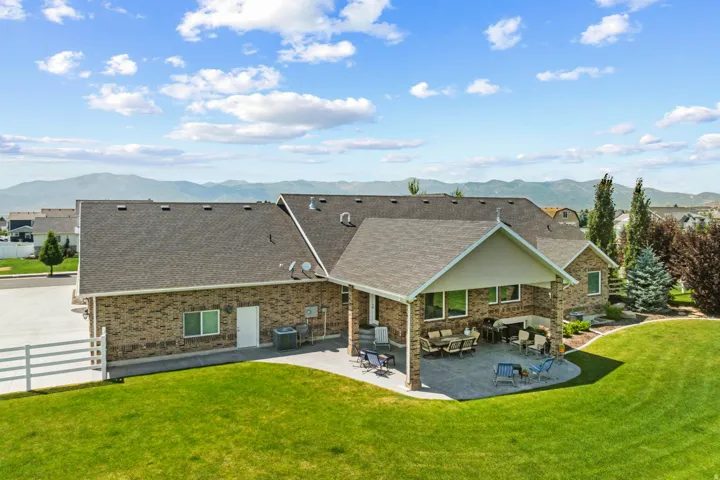 Rear exterior featuring a covered patio with stone columns, extensive paved patio space, and a expansive manicured lawn