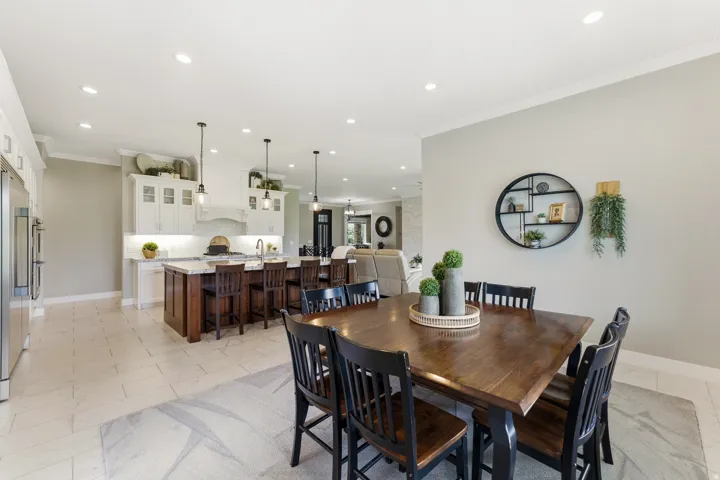 Open-concept kitchen and dining area featuring light-toned tile flooring, recessed lighting, and crown molding