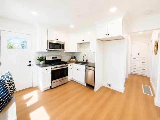 Kitchen featuring white shaker cabinetry, stainless steel appliances, dark countertops, a white subway tile backsplash, and wood-finish flooring
