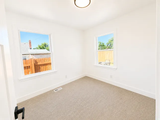 Bright room featuring two large windows, neutral carpet flooring, white baseboards, and a contemporary flush-mount ceiling light