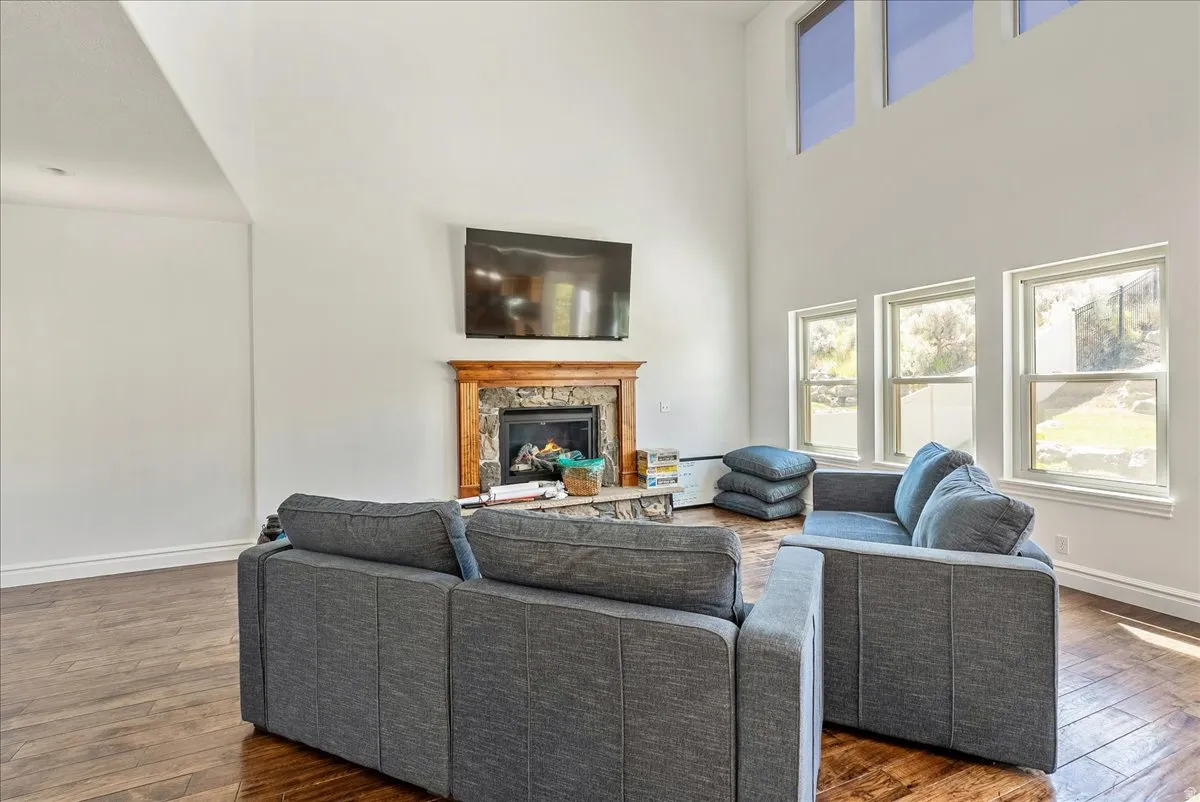 Spacious room featuring high vaulted ceilings, an integrated fireplace with a stone surround and wood mantel, multiple windows, and wood-finish flooring