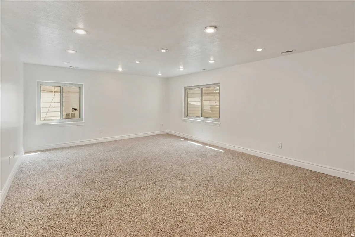 Spacious room featuring plush carpeting, white walls, recessed ceiling lights, and two windows