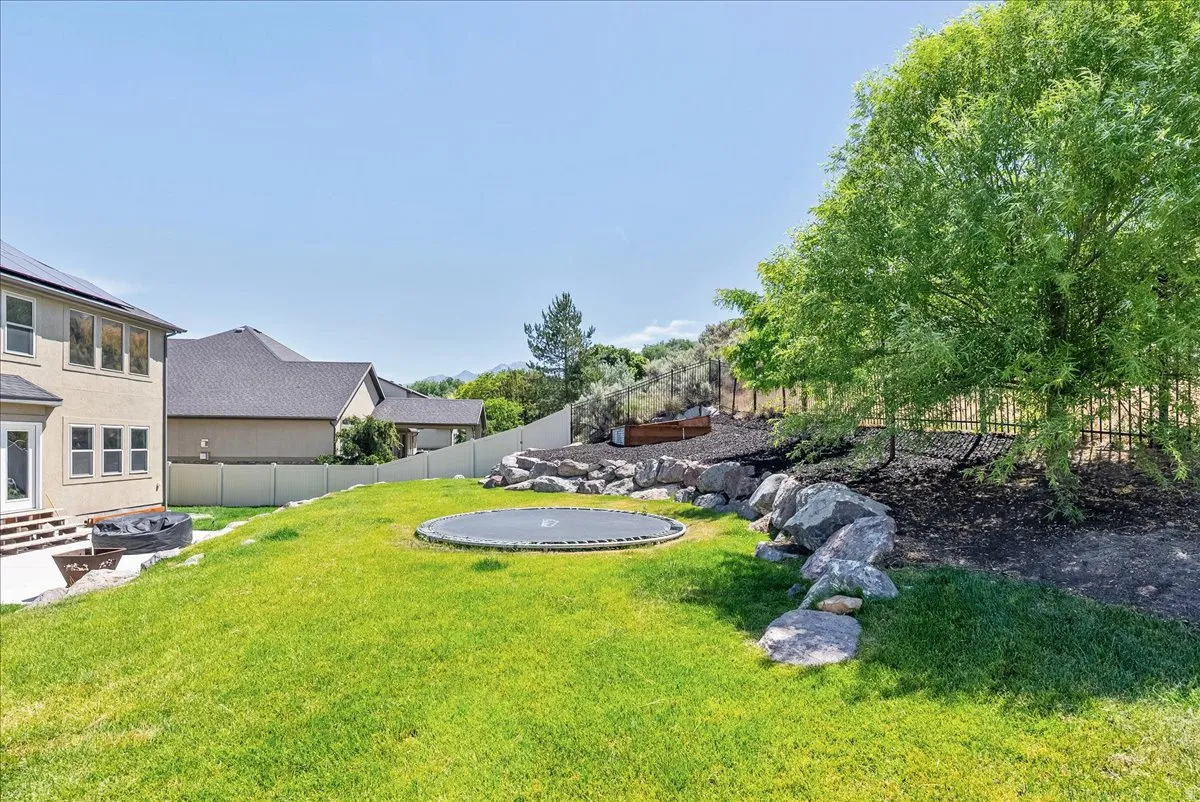Expansive green lawn with a rock retaining wall, mature trees, and a privacy fence