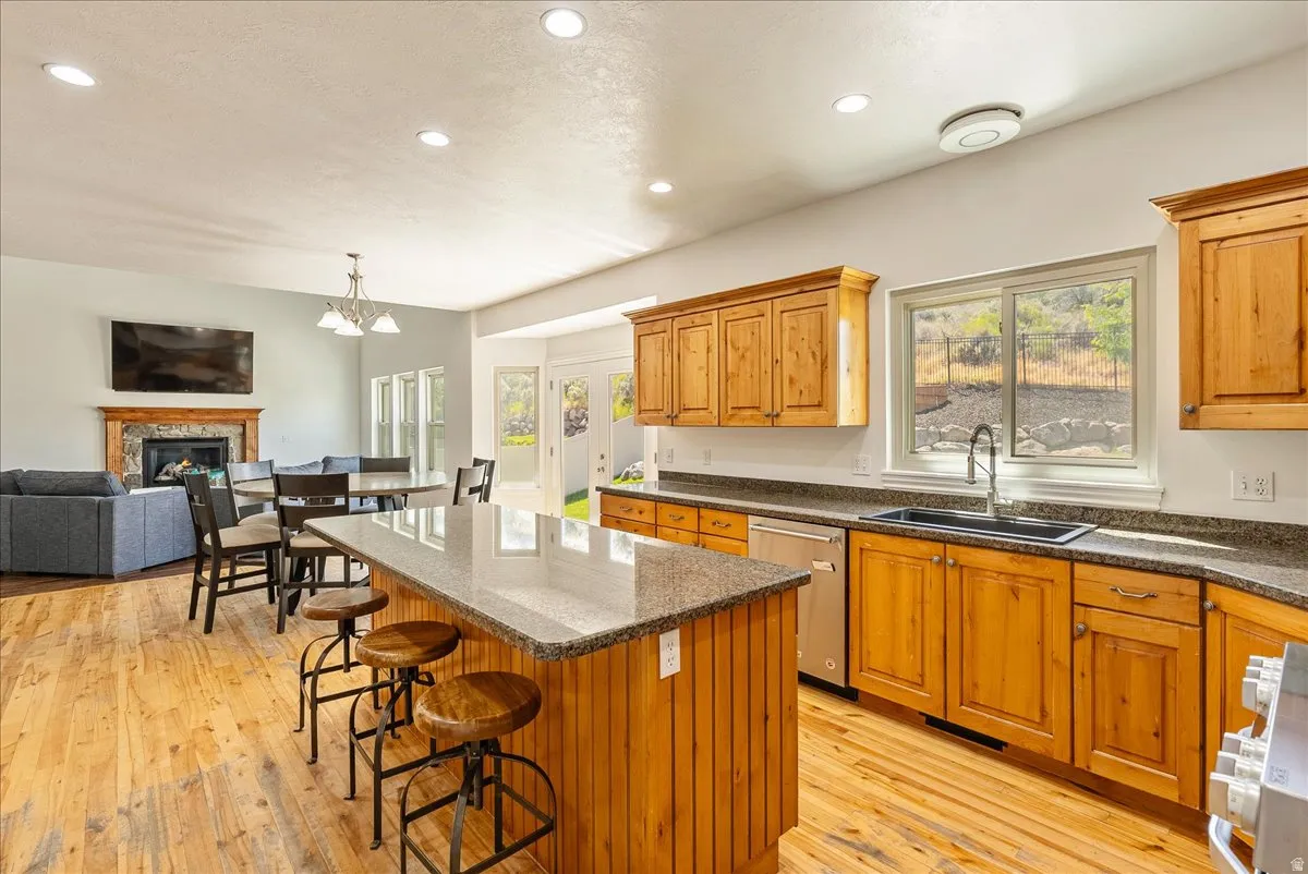 Open-concept kitchen featuring wood-finish flooring, a central island with a granite-style countertop, natural wood cabinetry, and stainless steel appliances