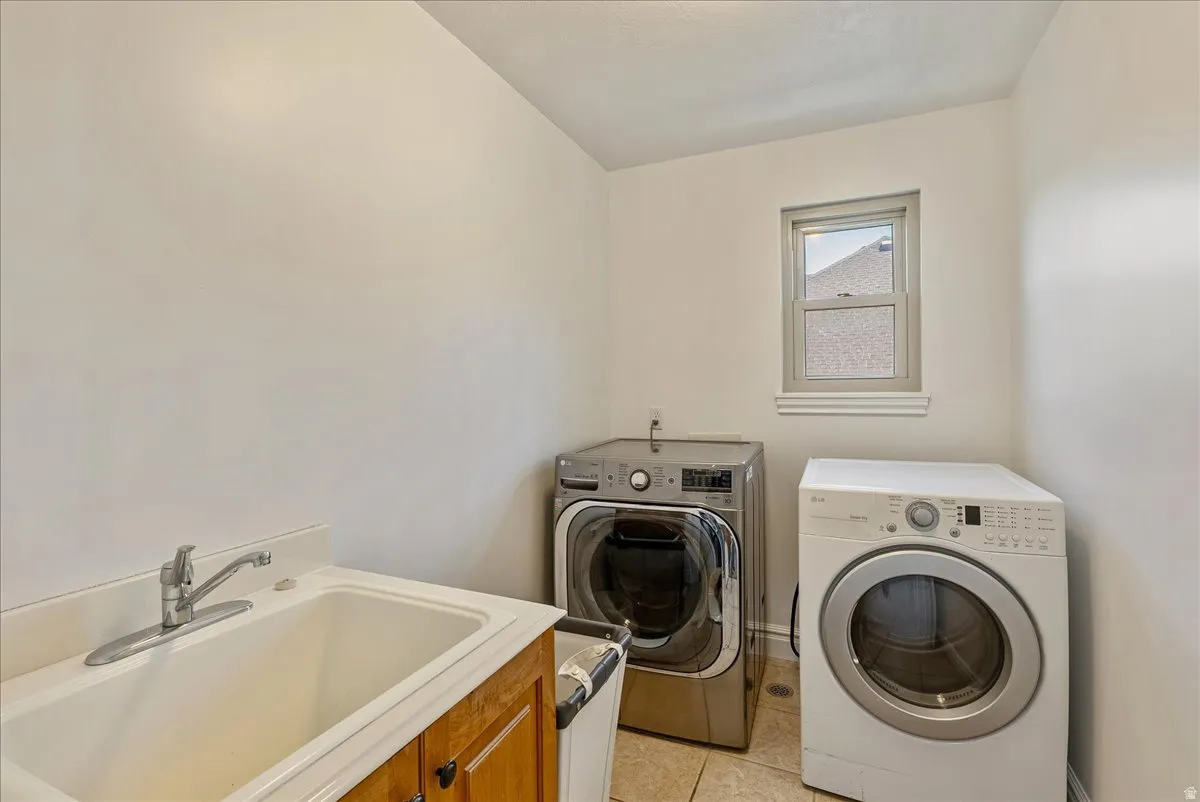 Dedicated laundry area featuring a utility sink with a chrome faucet, light wood cabinetry, and neutral tile flooring