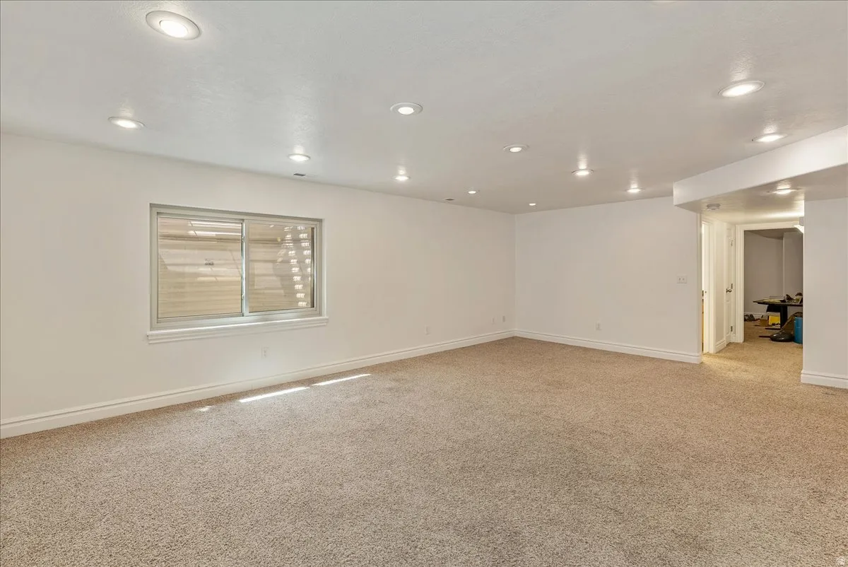 Spacious room featuring neutral carpet flooring, recessed lighting, white walls, and a sliding window with blinds
