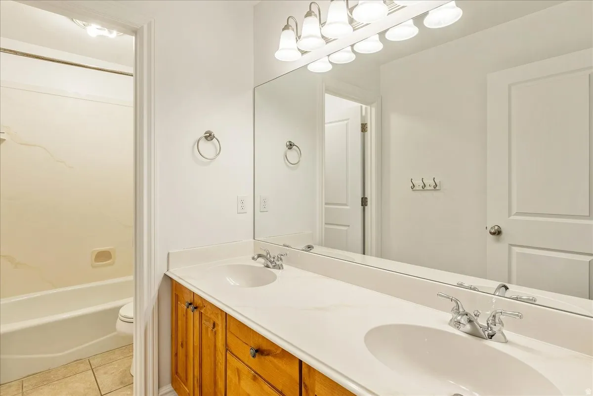 Bathroom featuring a dual-sink vanity with wood-finish cabinetry, a large wall-mounted mirror, and a multi-bulb vanity light fixture