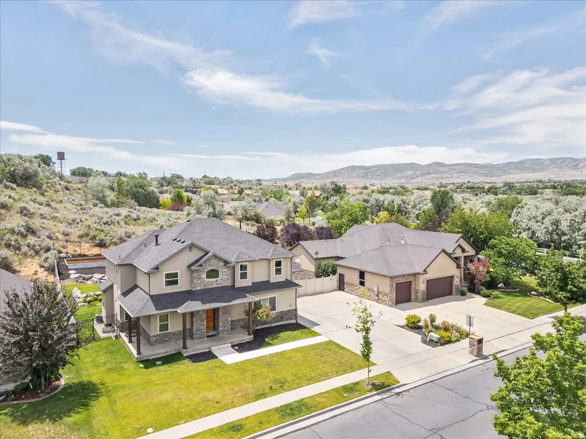 Two-story residence featuring a stone and stucco exterior, covered front porch, dark roof shingles, and a manicured front lawn