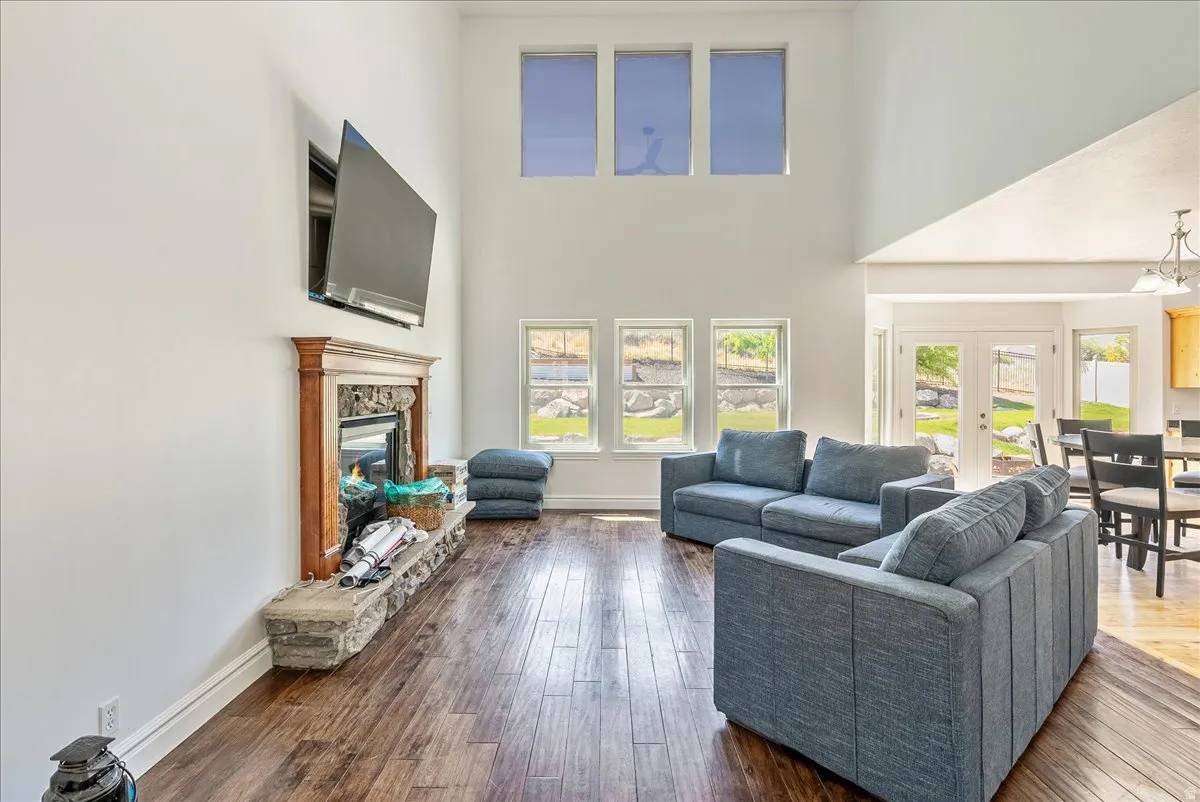 Spacious living area featuring a stone and wood-mantle fireplace, rich wood-finish flooring, and high vaulted ceilings