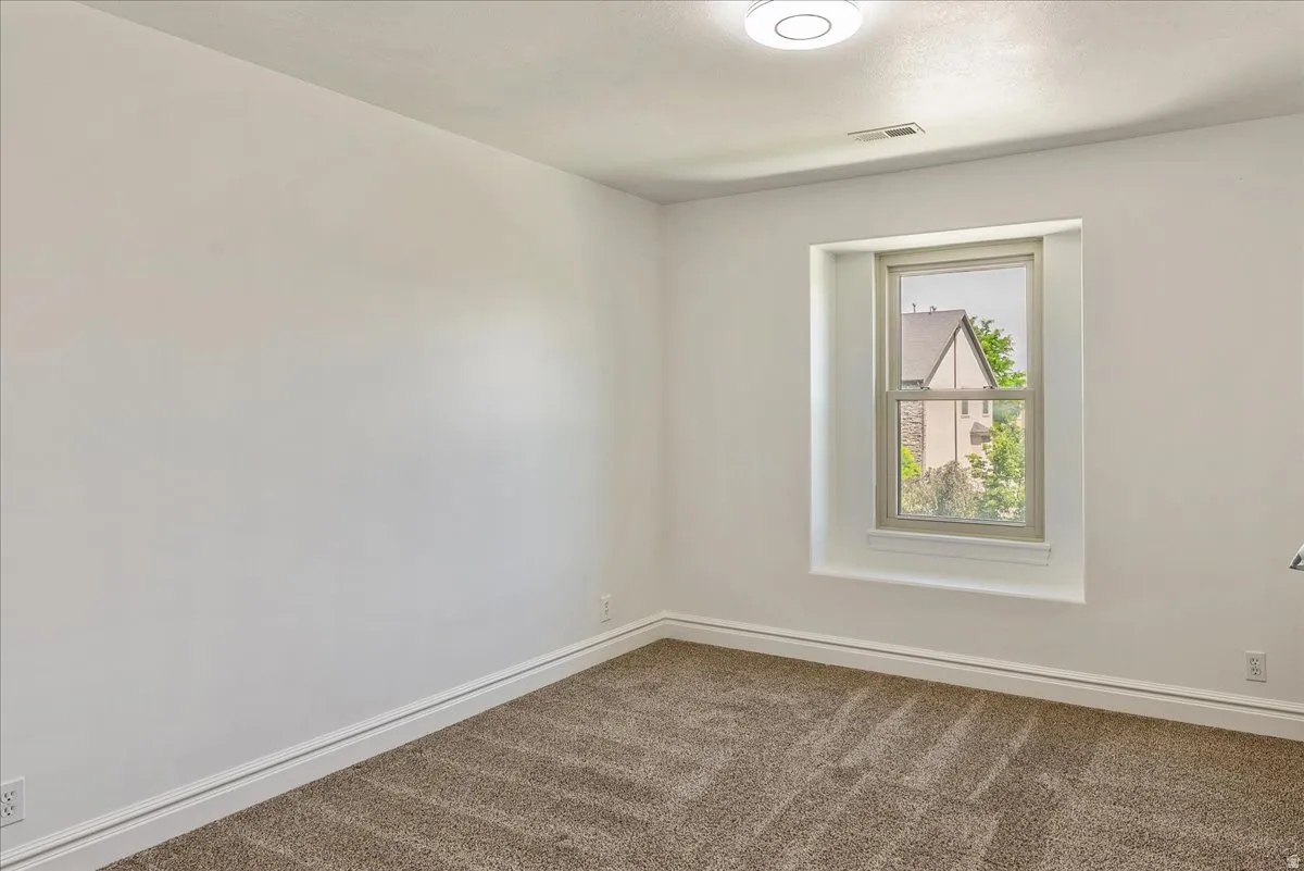 Bright room featuring a single window with white trim, tan carpet, white baseboards, and a flush-mount ceiling light