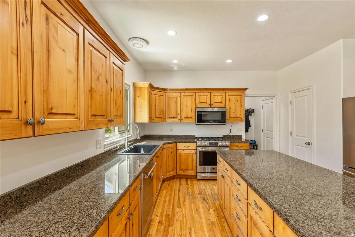 Kitchen featuring a long center island, wood-finish flooring, recessed lighting, and ample natural wood cabinetry with stone countertops