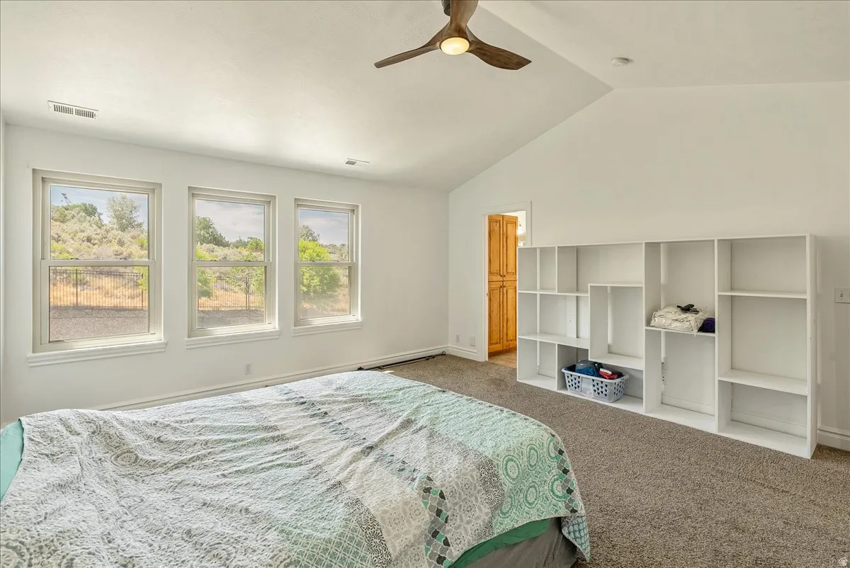 Vaulted ceiling room featuring three large windows, built-in shelving, a wood-finish ceiling fan with integrated lighting, and neutral tone carpeting