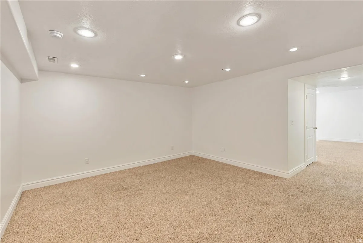 Spacious room featuring neutral carpeting, white baseboards, recessed ceiling lighting, and a neutral wall color