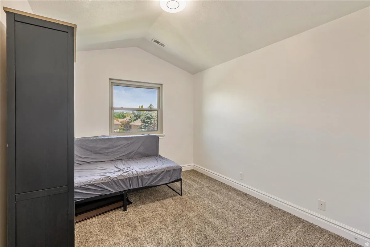 Bedroom featuring a window with exterior visibility, vaulted ceiling, neutral tone walls, and carpet flooring