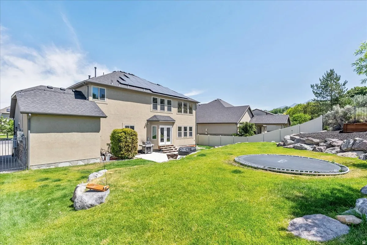 Expansive backyard featuring a stone patio, dual glass-paneled doors, and a terraced rock garden