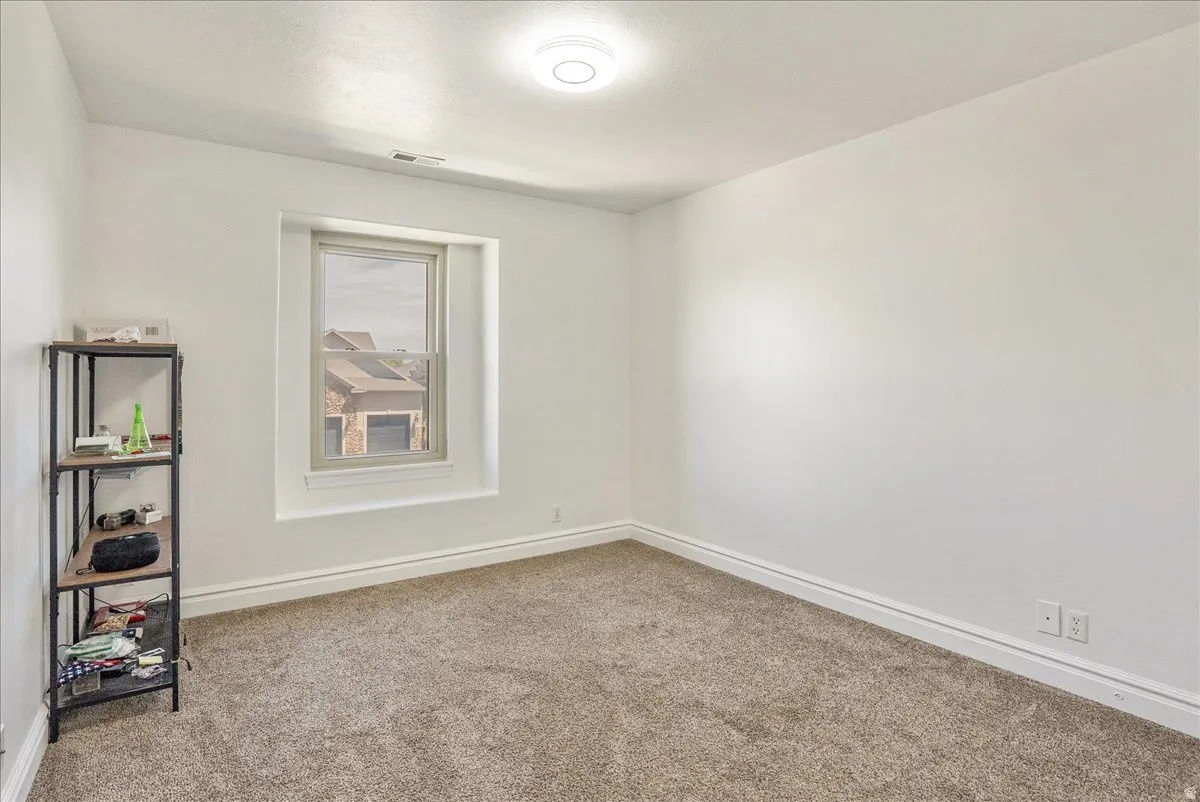 White walls, light brown carpet flooring, and a single window with white trim
