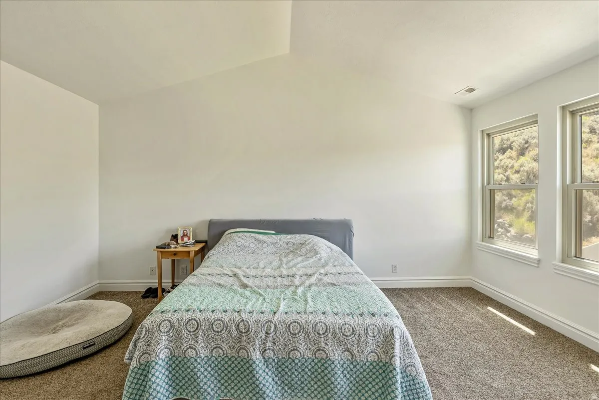 Vaulted ceiling room with two double-hung windows, light tan carpeting, and white baseboards