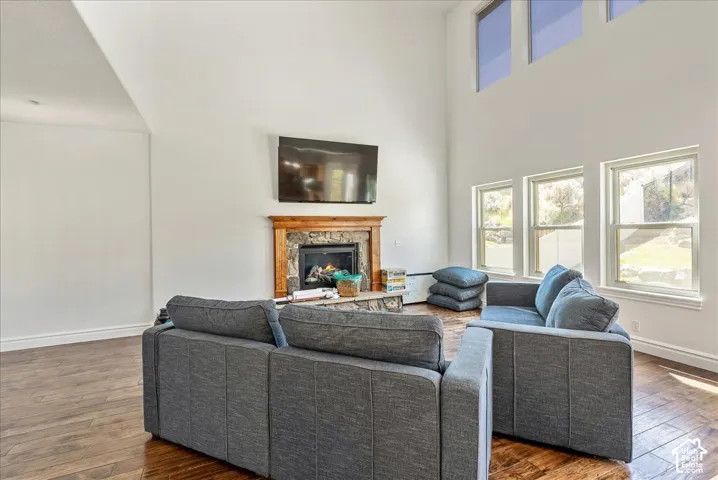 Spacious room featuring high vaulted ceilings, an integrated fireplace with a stone surround and wood mantel, multiple windows, and wood-finish flooring