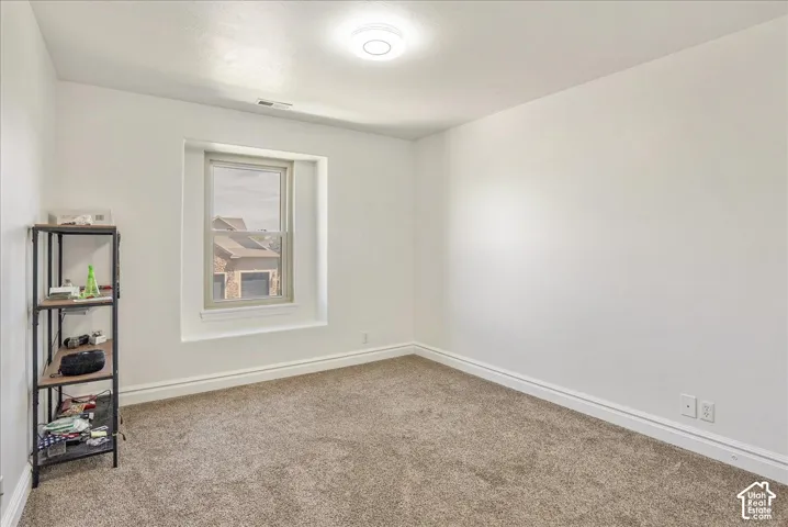 White walls, light brown carpet flooring, and a single window with white trim