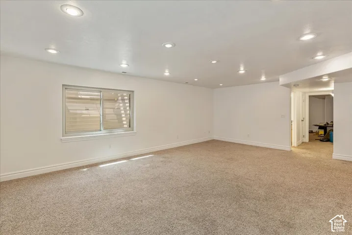 Spacious room featuring neutral carpet flooring, recessed lighting, white walls, and a sliding window with blinds