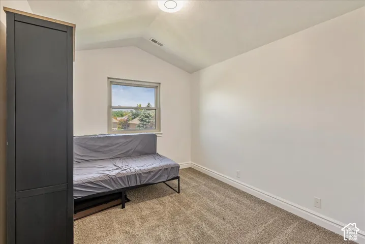 Bedroom featuring a window with exterior visibility, vaulted ceiling, neutral tone walls, and carpet flooring