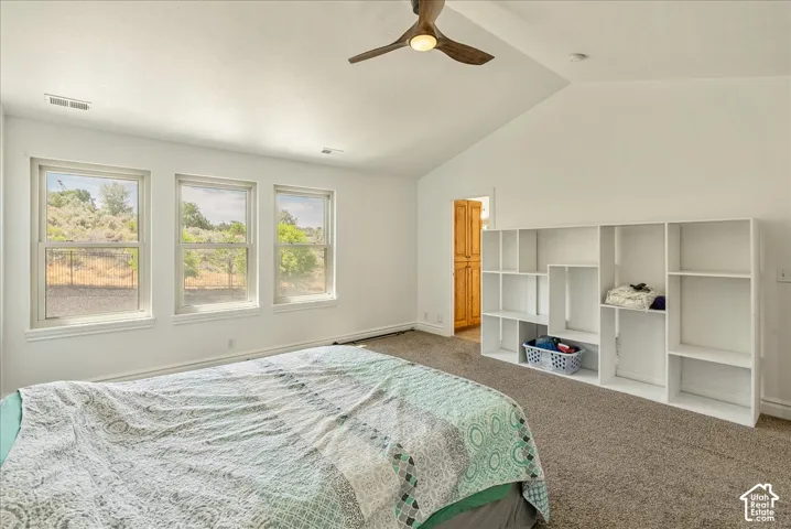 Vaulted ceiling room featuring three large windows, built-in shelving, a wood-finish ceiling fan with integrated lighting, and neutral tone carpeting