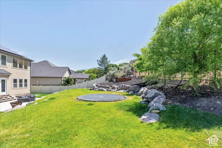 Expansive green lawn with a rock retaining wall, mature trees, and a privacy fence