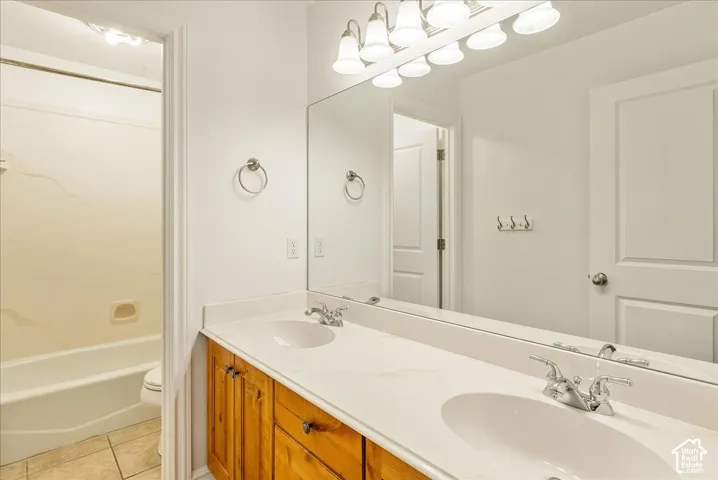 Bathroom featuring a dual-sink vanity with wood-finish cabinetry, a large wall-mounted mirror, and a multi-bulb vanity light fixture