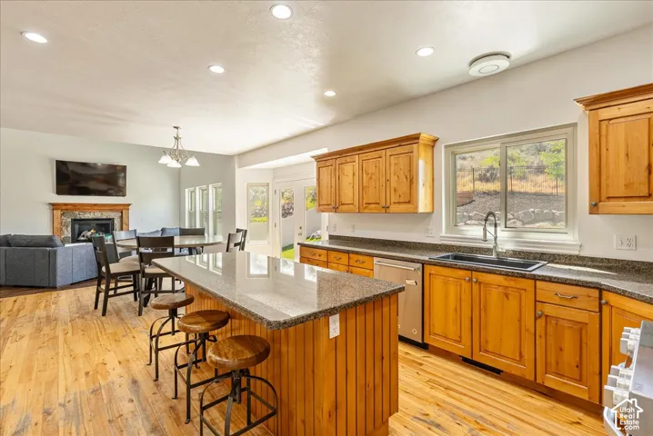 Open-concept kitchen featuring wood-finish flooring, a central island with a granite-style countertop, natural wood cabinetry, and stainless steel appliances