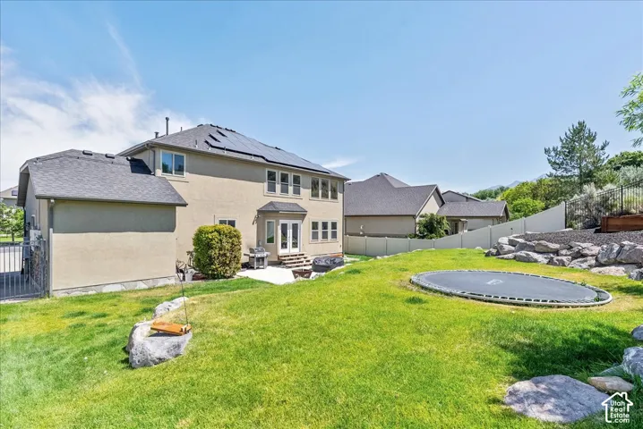Expansive backyard featuring a stone patio, dual glass-paneled doors, and a terraced rock garden