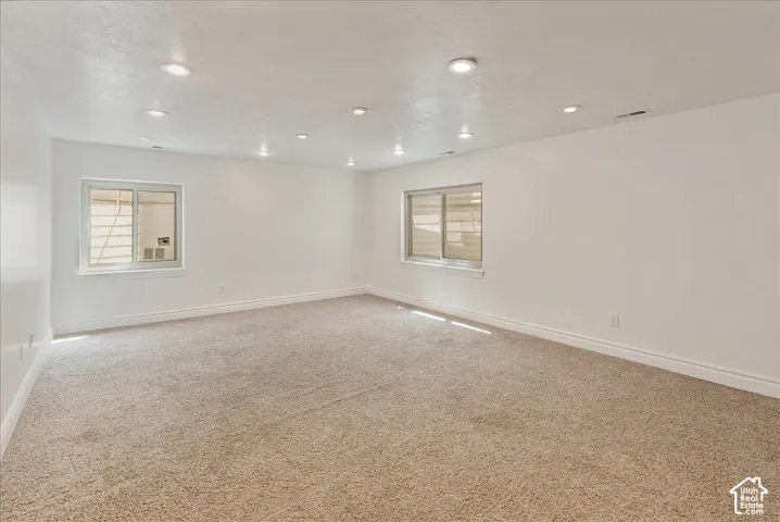 Spacious room featuring plush carpeting, white walls, recessed ceiling lights, and two windows