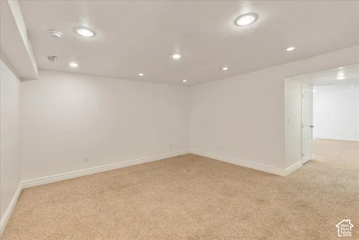 Spacious room featuring neutral carpeting, white baseboards, recessed ceiling lighting, and a neutral wall color
