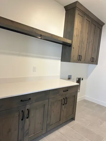 Wood-finish cabinetry with black hardware, white countertop, open shelving with hanging rod, and light-toned tile flooring