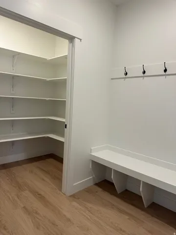 Walk-in pantry with extensive shelving, built-in bench seating, wood-finish flooring, and wall-mounted coat hooks