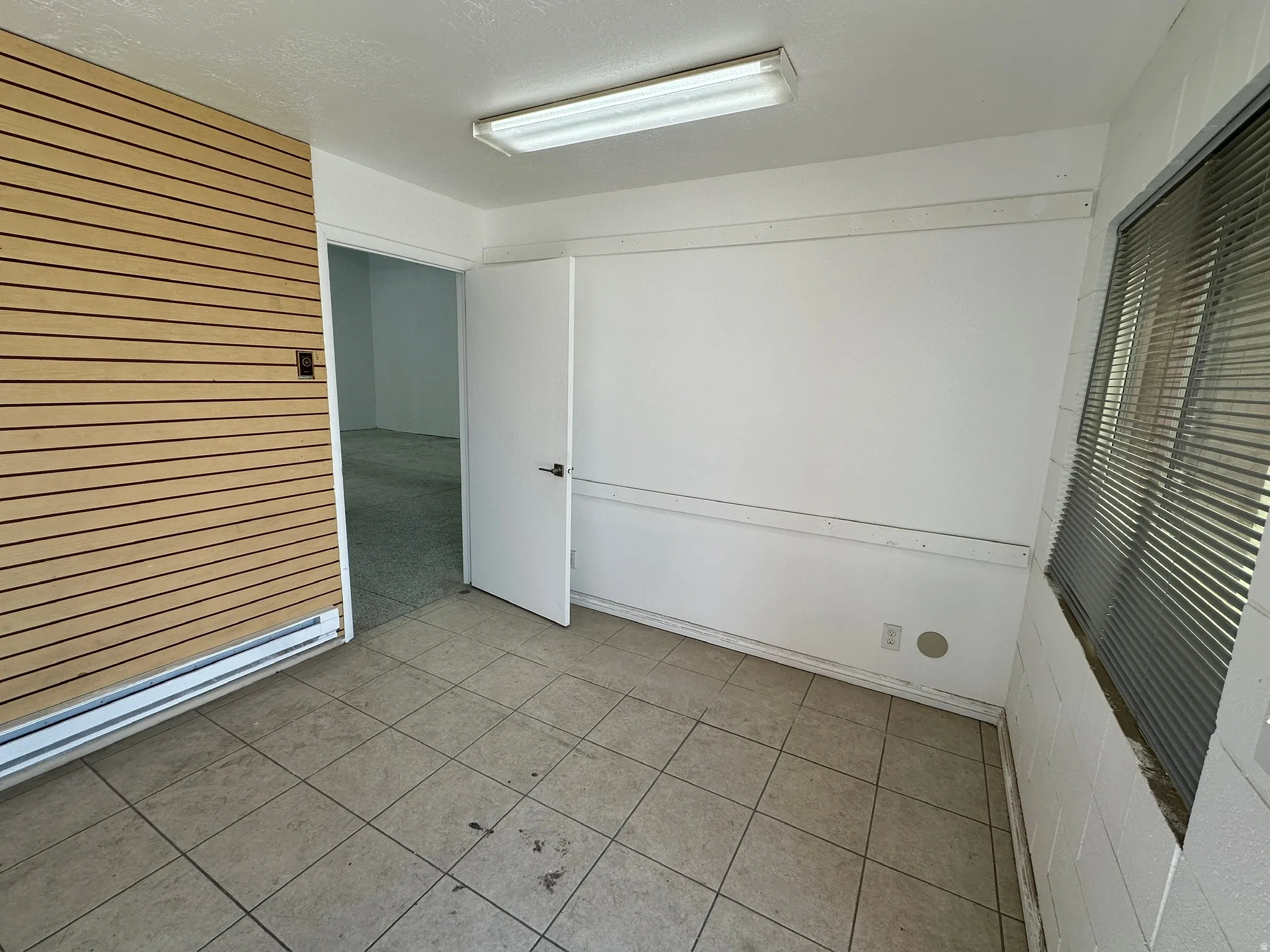 Commercial space featuring a slatwall panel, tile flooring, and a window with horizontal blinds