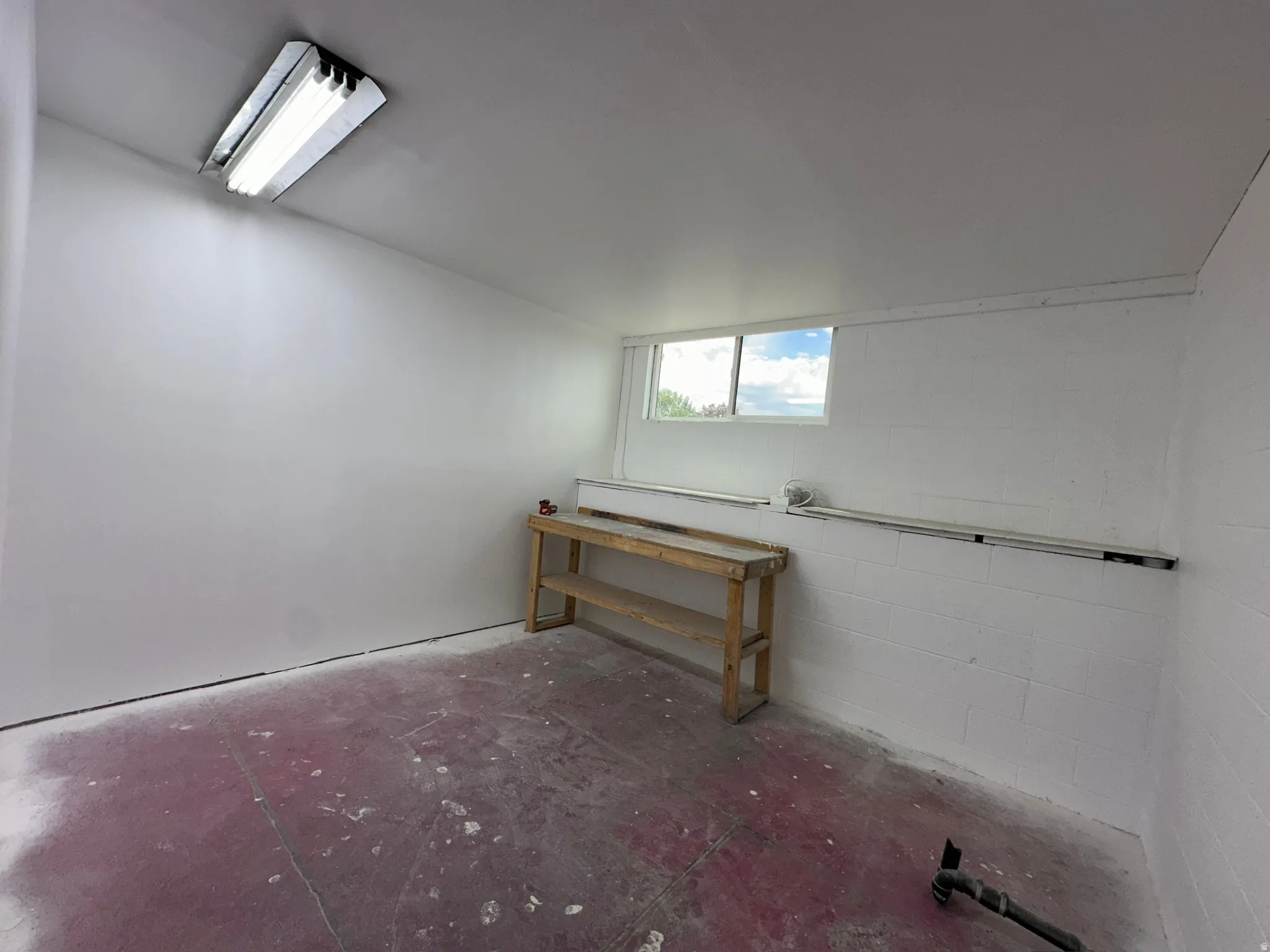 Basement space featuring a rectangular window, fluorescent ceiling light fixture, and painted concrete block walls