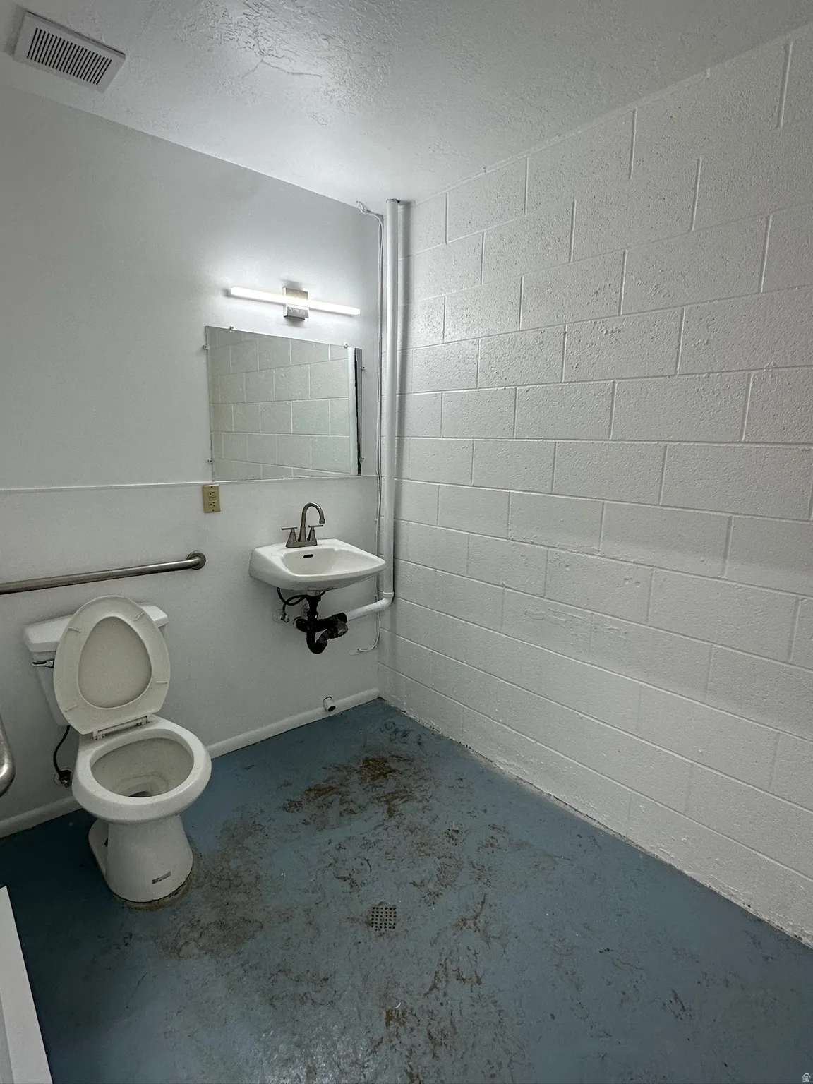 Restroom featuring a wall-mounted sink, mirror with vanity lighting, white toilet, and grab bars
